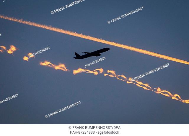 A passenger plane (top) crosses two condensation trails lightning up in red during sunset in Frankfurt/Main, Germany, 6 January 2017