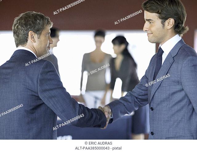 Executives standing, shaking hands in conference room