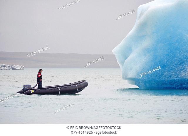 A man in a raft approaches an iceberg in Glacier Lagoon, Iceland