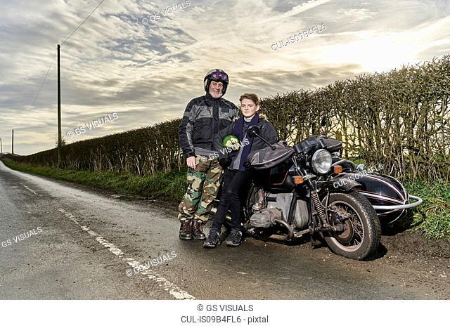 Portrait of senior male motorcyclist and grandson sitting on motorcycle at roadside