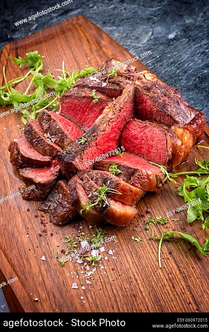 Modern style traditional barbecue dry aged wagyu porterhouse beef steak offered with lettuce and spice as close-up on modern design wooden board