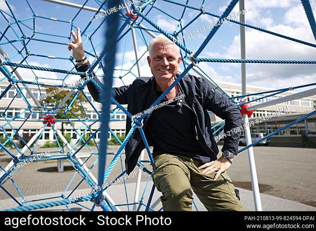 10 August 2021, North Rhine-Westphalia, Cologne: Guido Cantz, presenter, sits in a climbing frame in the schoolyard of Dee's Maximilian-Kolbe-Gymnasium