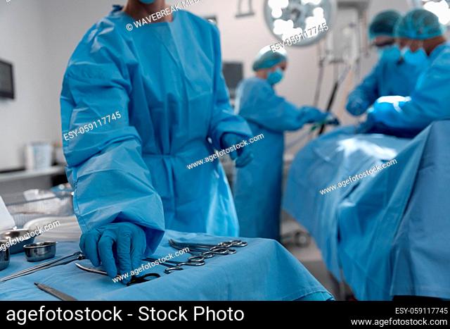 Midsection of female surgeon reaching for surgical scissors in operating theatre