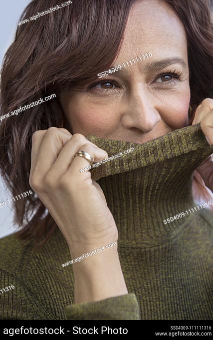 Close up of a middle-aged red head woman covering her face with her turtle neck sweater