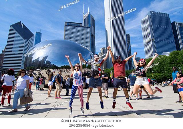 Chicago Illinois Millennium Park July 4th locals jumping for joy at Cloud Gate sculpture called The Bean with skyline in background skyscrapers in downtown...