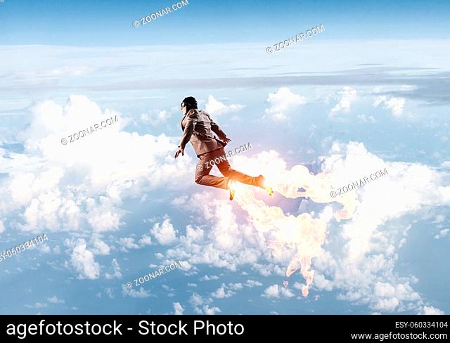 Businessman in suit and aviator hat flying in blue sky as superhero. Corporate manager as superman launching upwards with jet flame in stratosphere