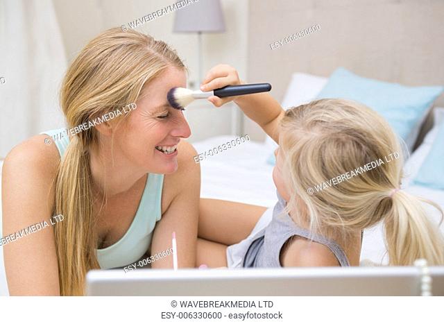 Cute little girl and mother on bed using laptop at home in the bedroom