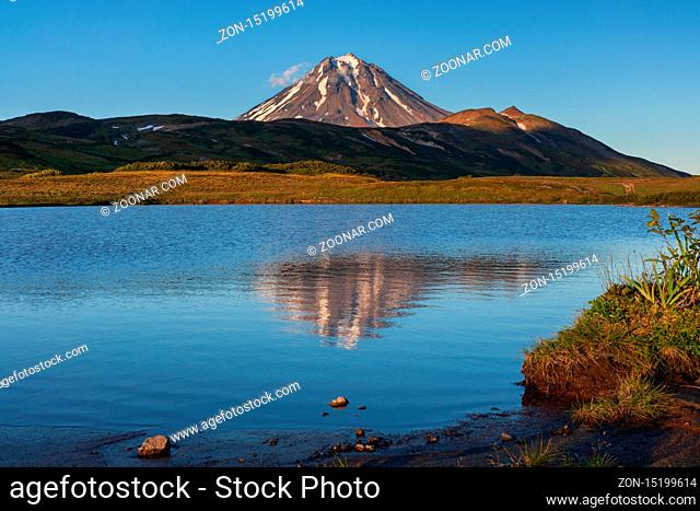 Stunning autumn volcano landscape of Kamchatka Peninsula at sunset: scenery evening view of cone Vilyuchinsky Volcano and reflection of mountains in picturesque...