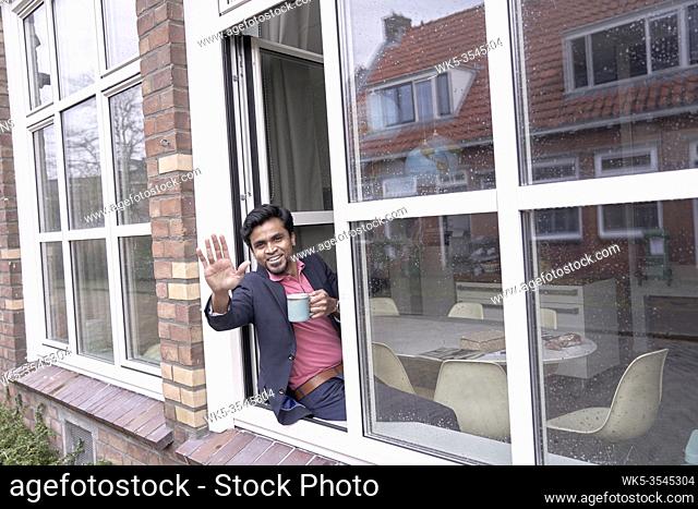 successful Indian man waving from the window of his modern apartment