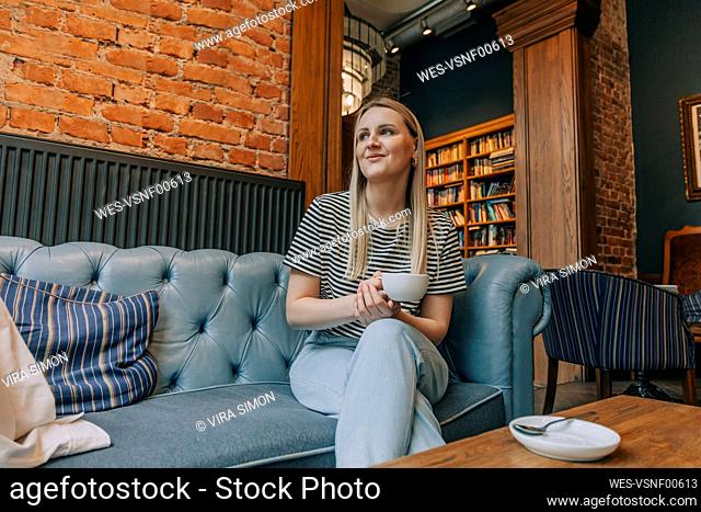 Smiling woman sitting with coffee cup on couch in cafe
