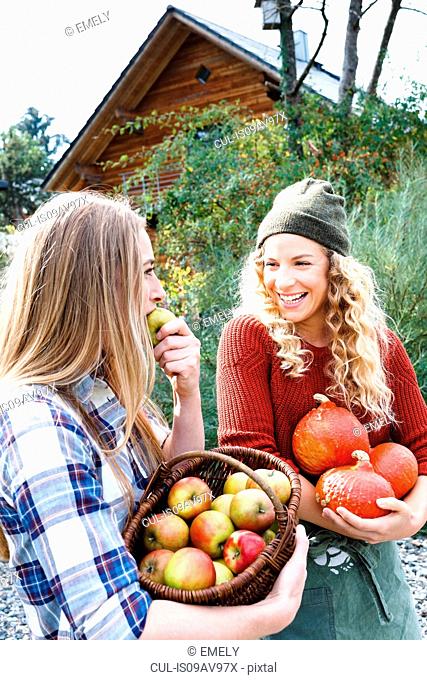 Two friends carrying homegrown produce, one woman eating apple