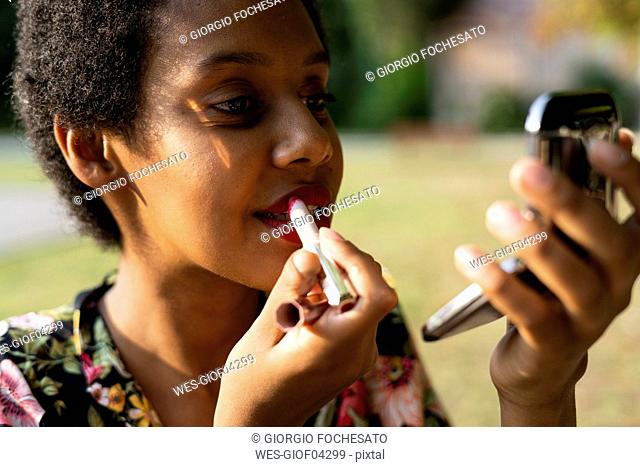 Portrait of young woman applying lipstick outdoors