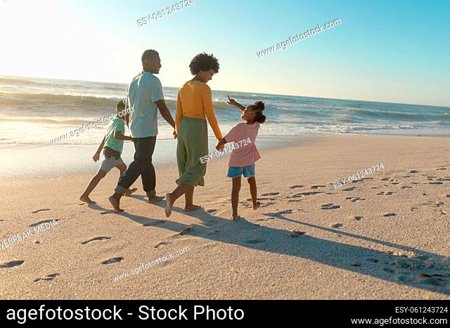 African american parents walking with children while holding hands at beach on sunny day