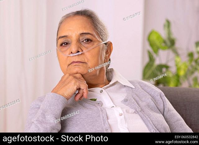 Old woman sitting on sofa with nasal cannula at home