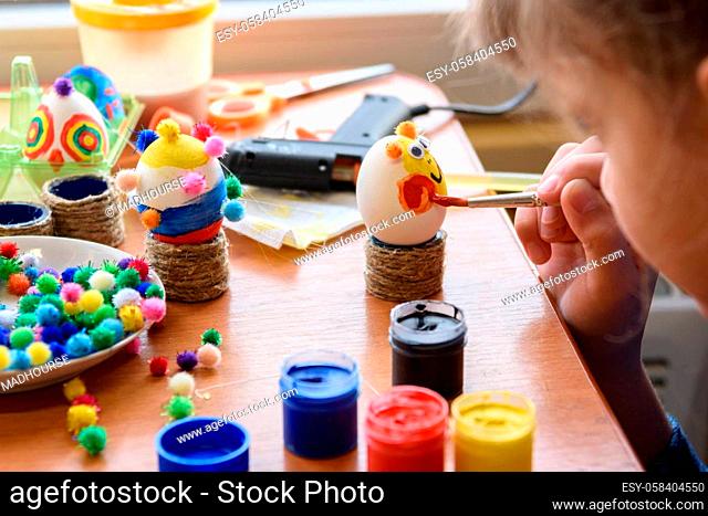 Girl carefully and neatly paints Easter eggs, close-up
