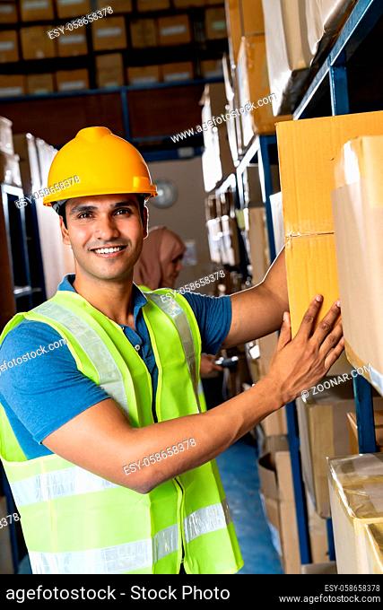 Portrait of Indian warehouse worker put cardboard box in to shelf with muslim asian worker do inventory in warehouse distribution center environment