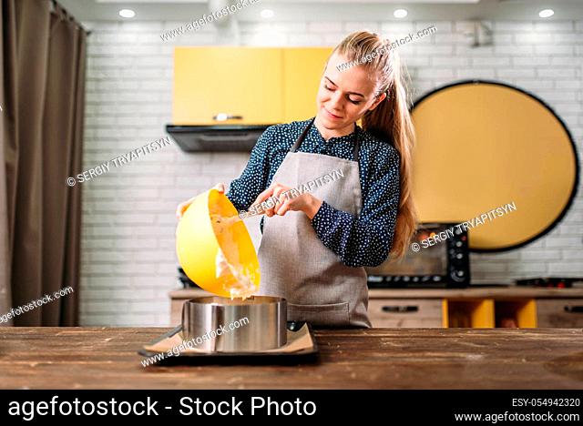 Woman cook in apron adds cream for the cake into the pan. Kitchen on background