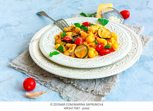 Plate of delicious pasta with tomato, zucchini, cheese and fresh mint on a grey textured background