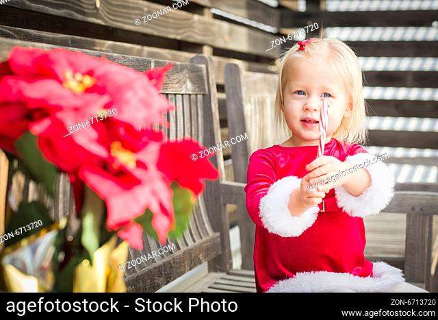 Adorable Little Girl Sitting On A Bench with Her Candy Cane Outside