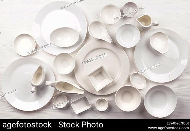 Set of empty dishware on white background with copy space, clean tableware assortment on wooden table, top view