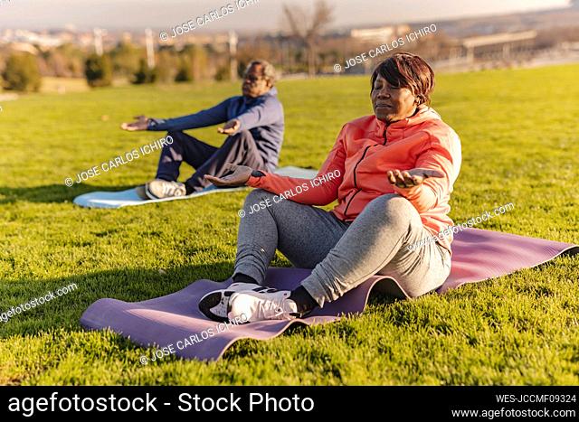 Senior woman practicing yoga with man in background