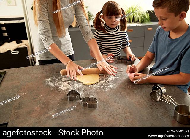 Hands of girl rolling dough by sister and brother at home