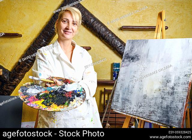 Satisfied female artist posing near new picture next to easel. High quality photo