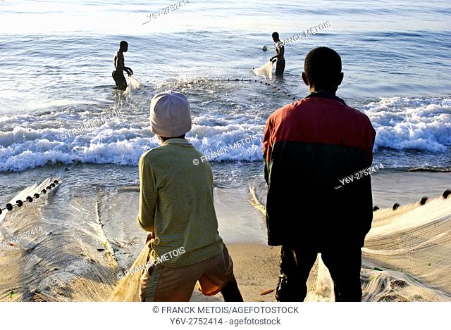 Boys are pulling a fishing net out of the water. Two fishermen are helping them. At Toamasina ( Madagascar)
