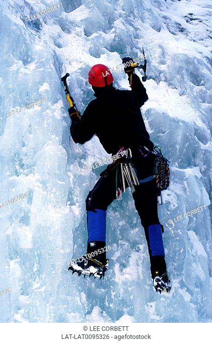 Rockies. Steep cliff face. Ice, frozen waterfall. Man climbing up face with ropes, ice axe. Ice climbing