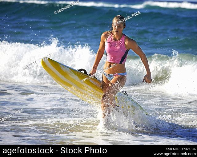 Female surf lifeguard training and running out of the sea holding ocean surf ski