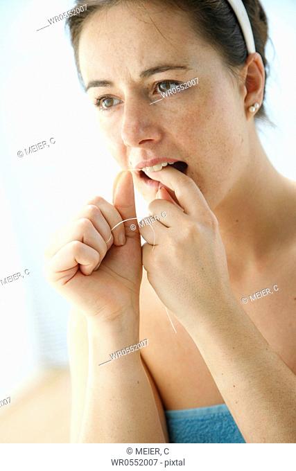 young woman dressed in a towel cleaning her teeth with dental floss