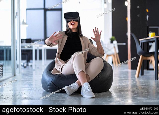 Female professional gesturing while enjoying virtual reality on bean bag in coworking office
