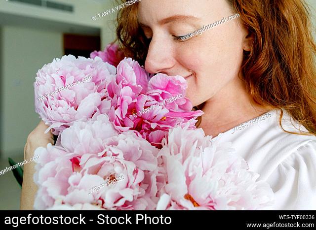 Smiling woman smelling pink flowers at home