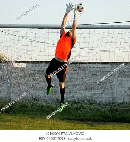 The goalkeeper is jumping high to the soccer ball, playing soccer