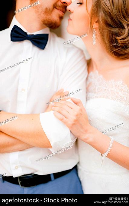 The groom folded his arms over his chest, the bride gently hugs him by the elbow and is about to kiss, close-up. High quality photo