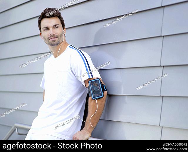 Jogger with earphones leaning at a wall
