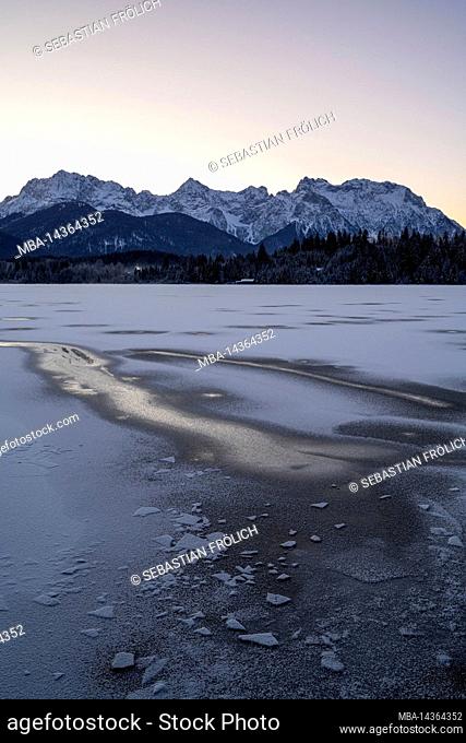 The frozen Barmsee near Krün in the Bavarian foothills of the Alps. In the foreground a track in the ice, in the background forest