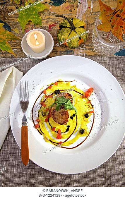 Seared scallops in saffron sauce with truffles on white plates on country table, with a candle and fall decorations