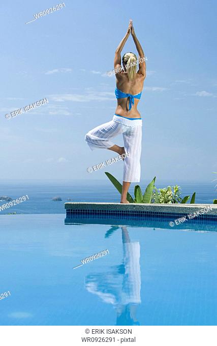Mid adult woman standing in a tree pose at the poolside