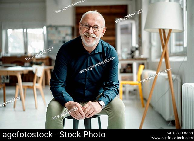 Happy senior businessman sitting on stool in office