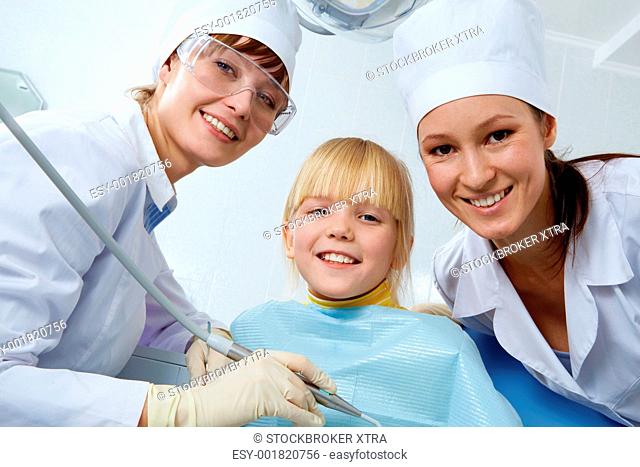 Group of dentist, assistant and little girl looking at camera
