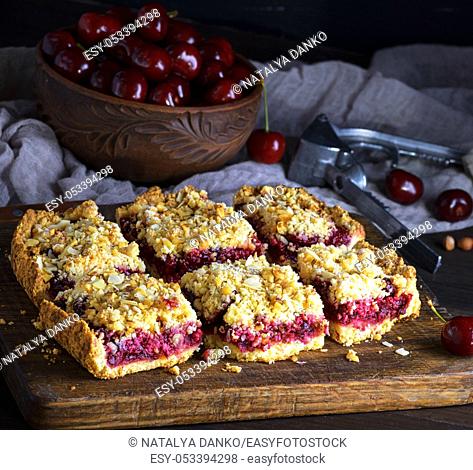 square pieces of cake crumble with cherry on brown wooden board, top view,