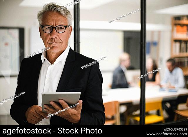 Senior businessman using digital tablet, coworkers working in background