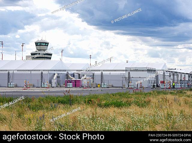 PRODUCTION - 12 July 2023, Berlin: The tower of the former Berlin-Tegel Airport behind the tents currently housing refugees