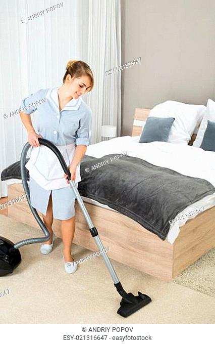 Happy Female Housekeeper Cleaning Floor With Vacuum Cleaner In Hotel Room