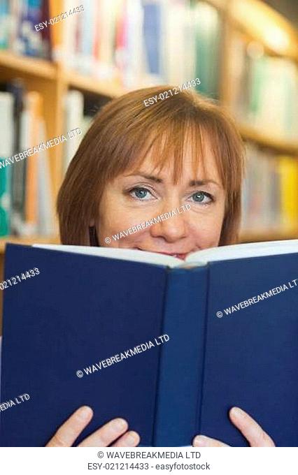 Content mature woman sitting in library holding a book