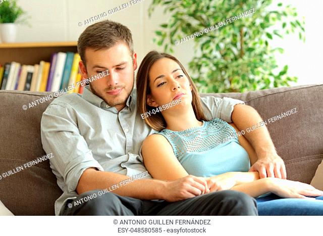 Bored couple wasting time sitting on a sofa at home