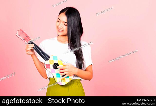 Portrait of happy Asian beautiful young woman teen confident smiling face hold acoustic Ukulele guitar, female playing Hawaiian small guitar