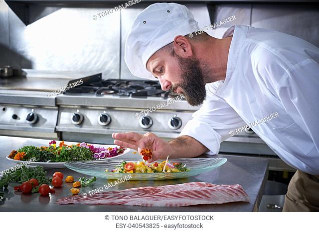 Chef garnishing flower in ceviche dish with hands at stainless steel kitchen