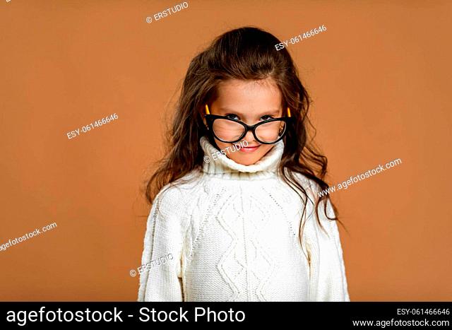 Cute curly little girl wearing glasses and looking to camera in studio. child stares